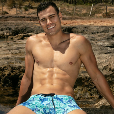 Man wearing blue swim trunks with a tropical background